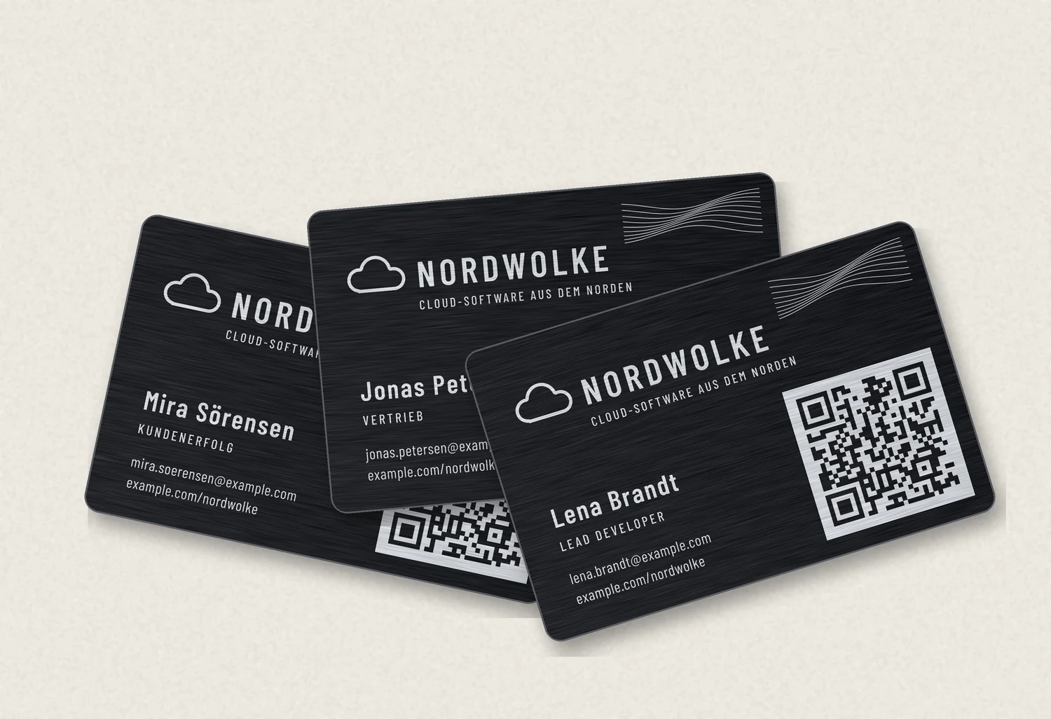 Drei schwarze Metall-Visitenkarten der Firma Nordwolke, aufgefächert, mit silbern gravierten Namen, Nordlicht-Linien und QR-Code